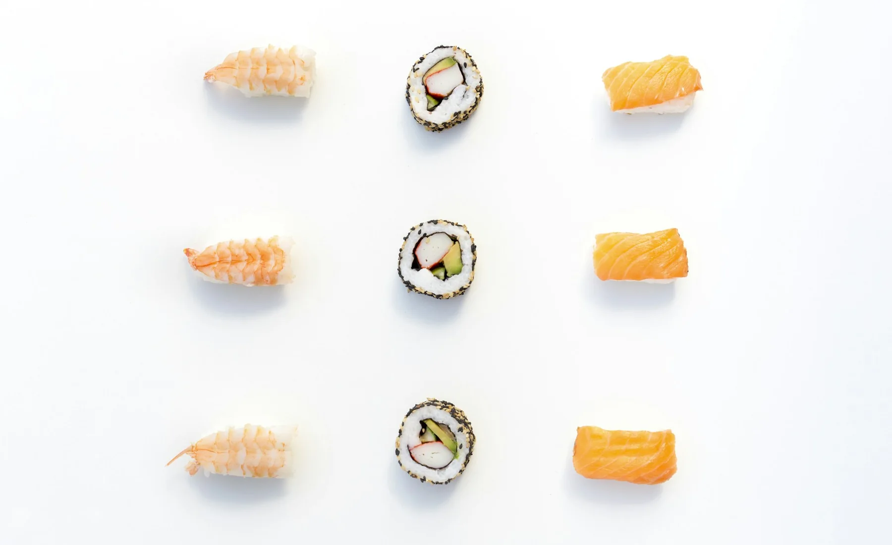 Nio bitar sushi i tre rader på vit botten, fotograferade rakt uppifrån