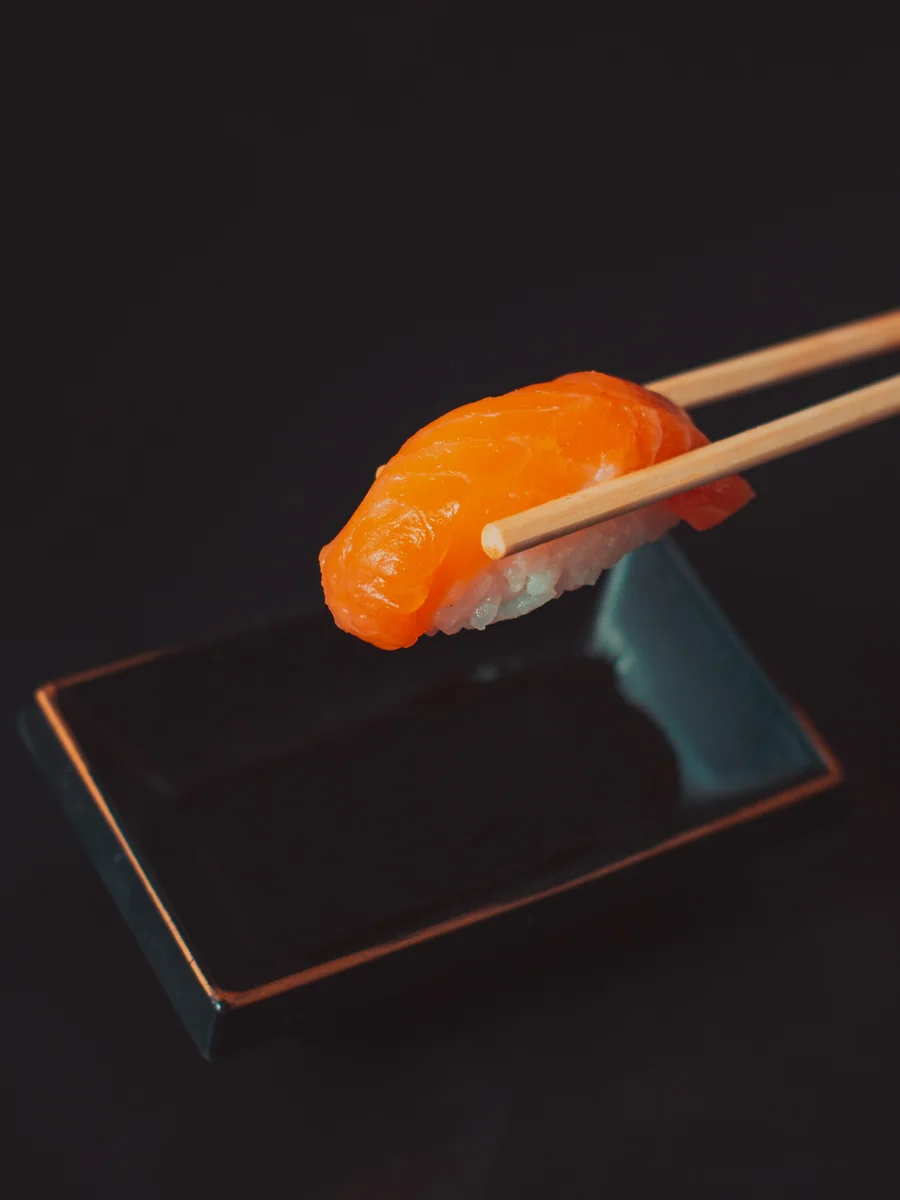 Ätpinnar lyfter en laxnigiri över ett svart fat
