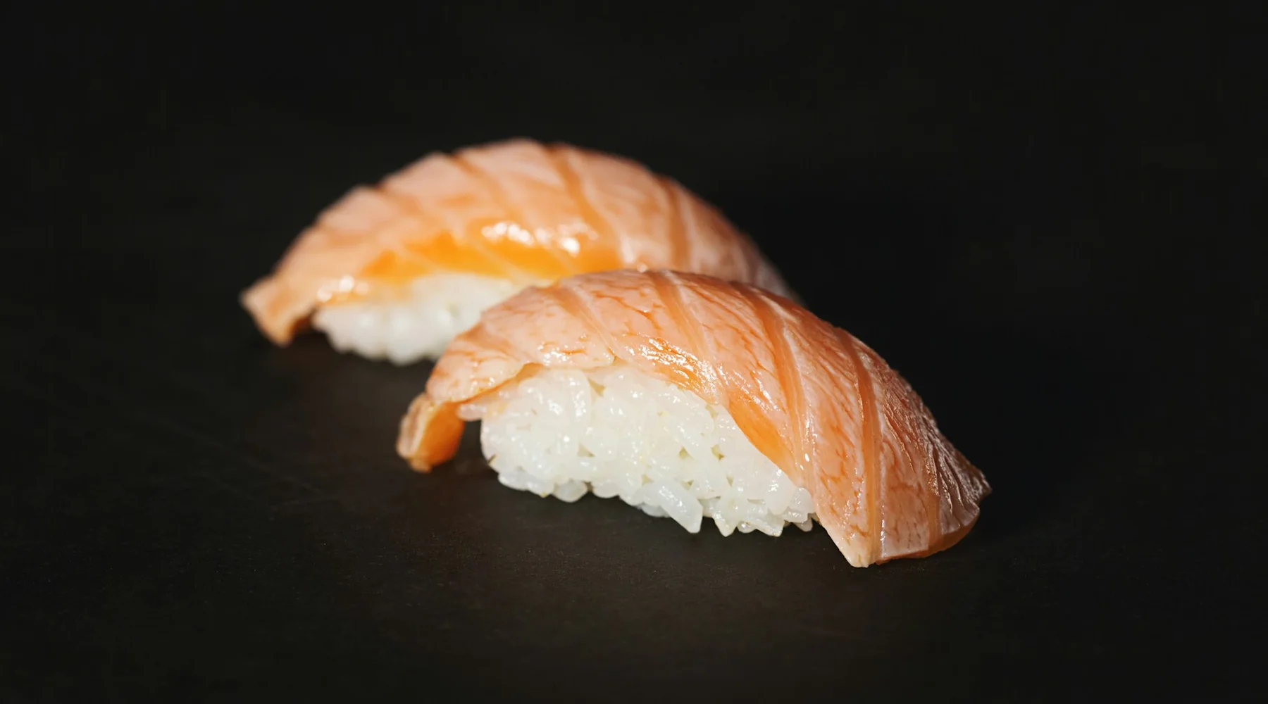 Två laxnigiri på svart botten