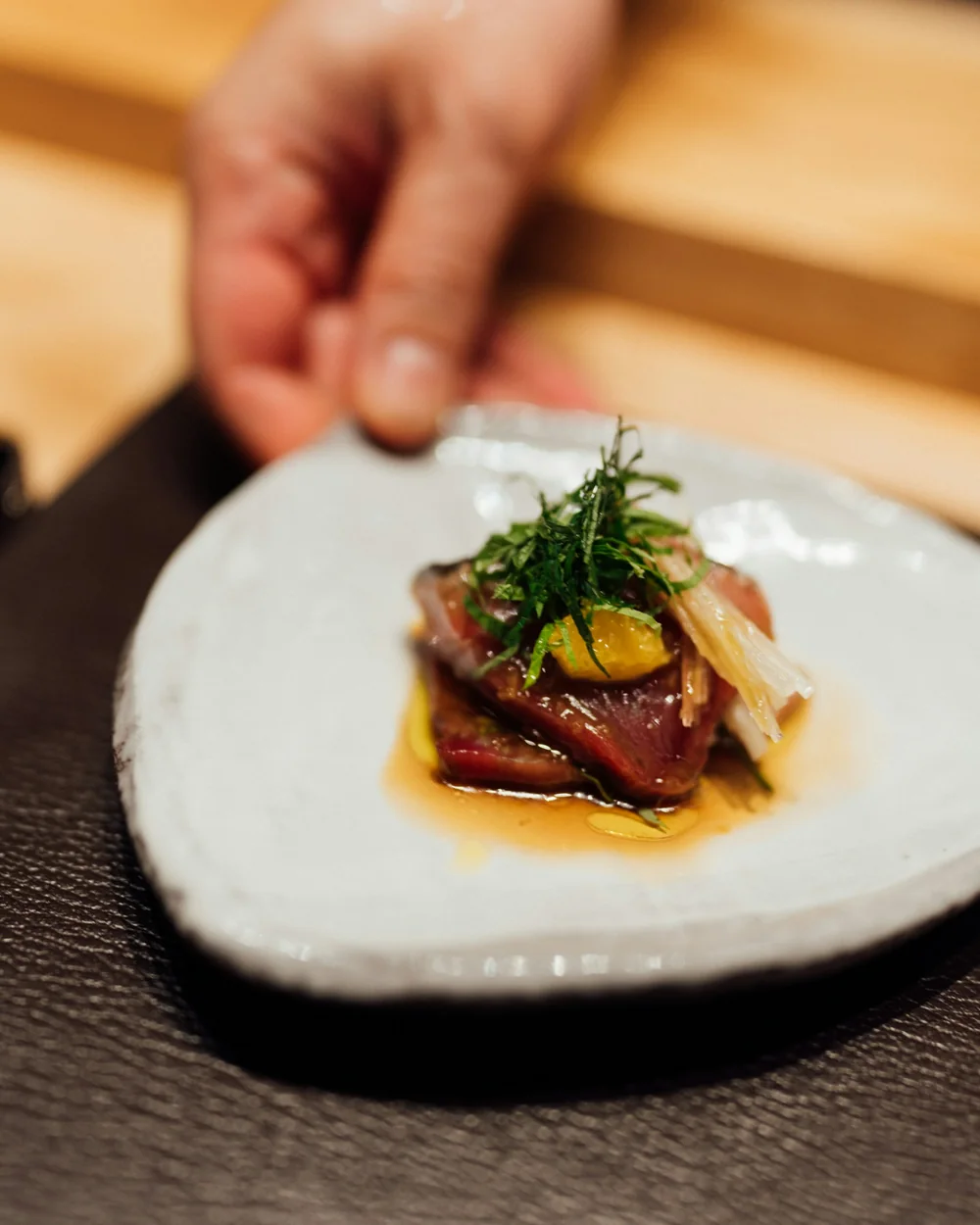 En hand ställer fram ett vitt fat med en enda bit fisk