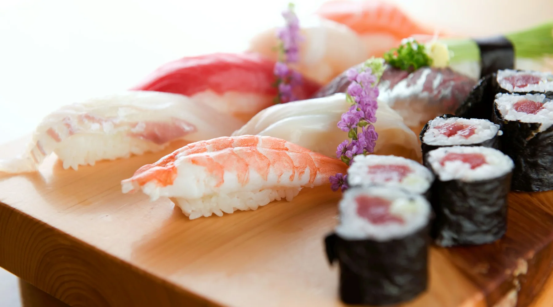 Ett ljust träbord fullt med nigiri och rullar i dagsljus