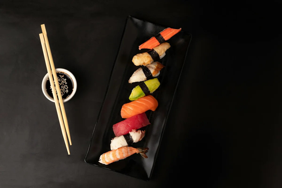 Ett svart avlångt fat med nigiri och ett par ätpinnar