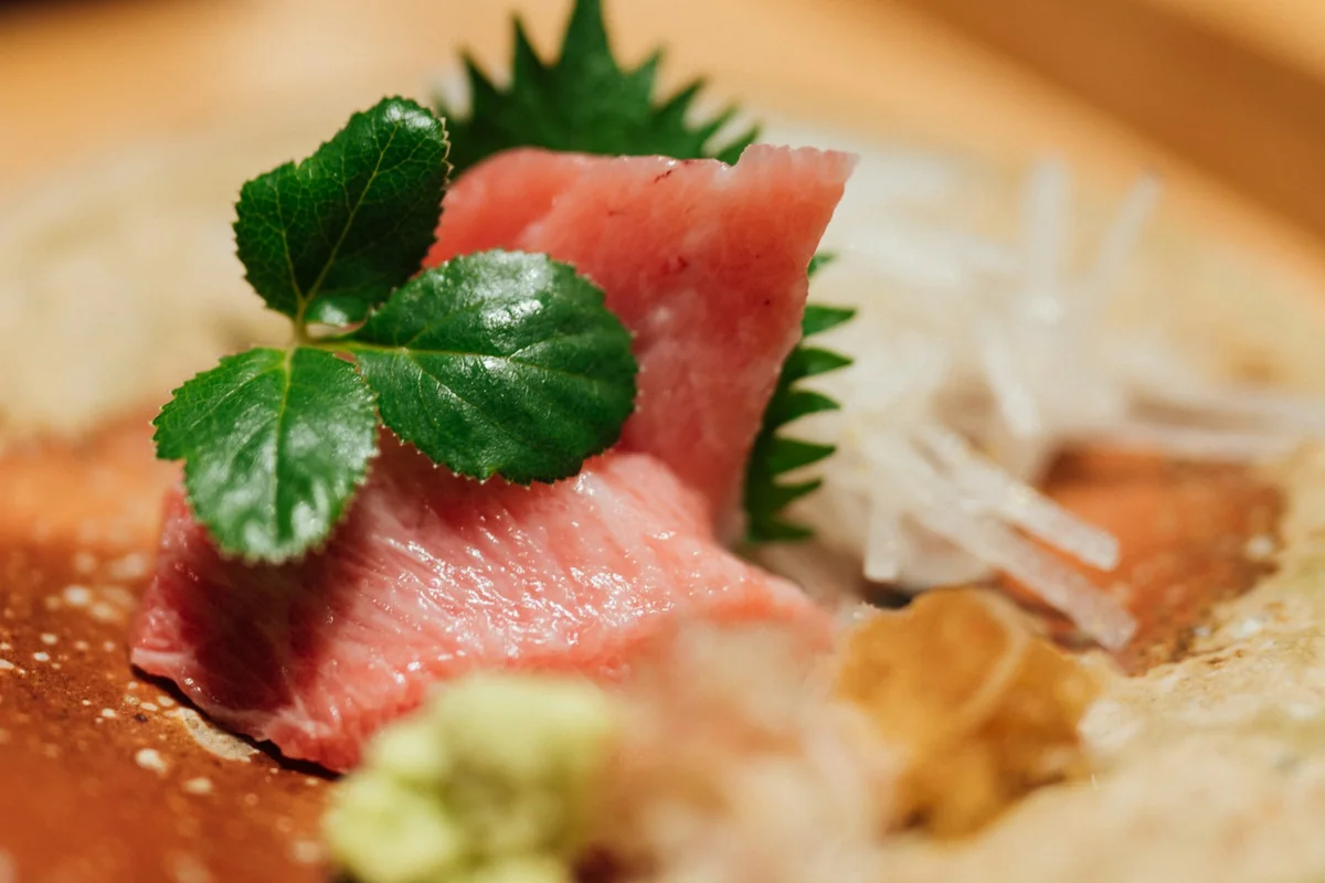 Sashimi med gröna blad på ett ljust keramikfat