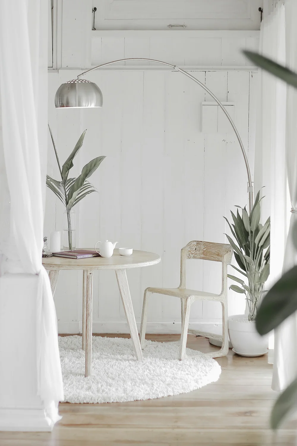 Minimalistiskt vitt rum med b&aring;gf&ouml;nster och ett litet bord