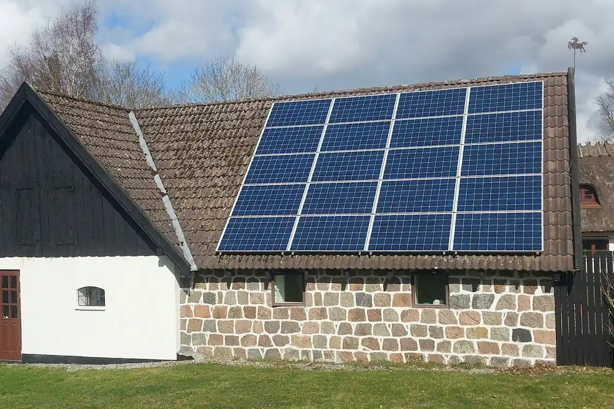 Solceller på taket till ett vitkalkat gårdshus med stenmur