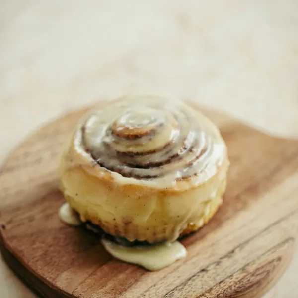 SMULA bageri (demo) 3 En kanelbulle med glasyr på en rund träbricka